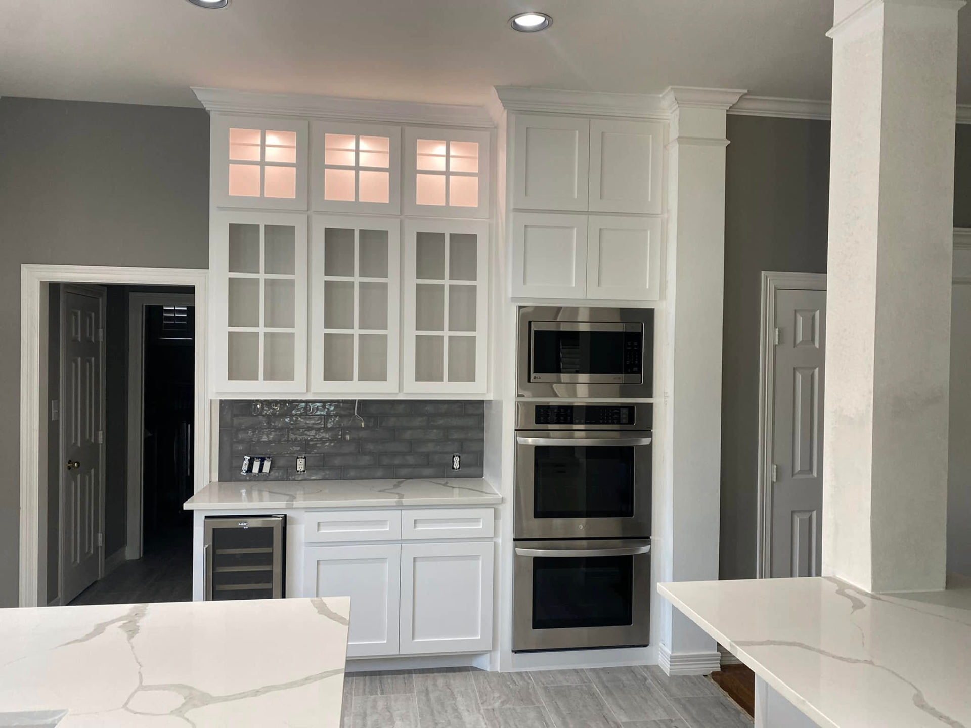 Butler's pantry with glass display cabinets Custom white cabinetry with glass display uppers, double wall oven, and Calacatta quartz counters in Fulshear TX