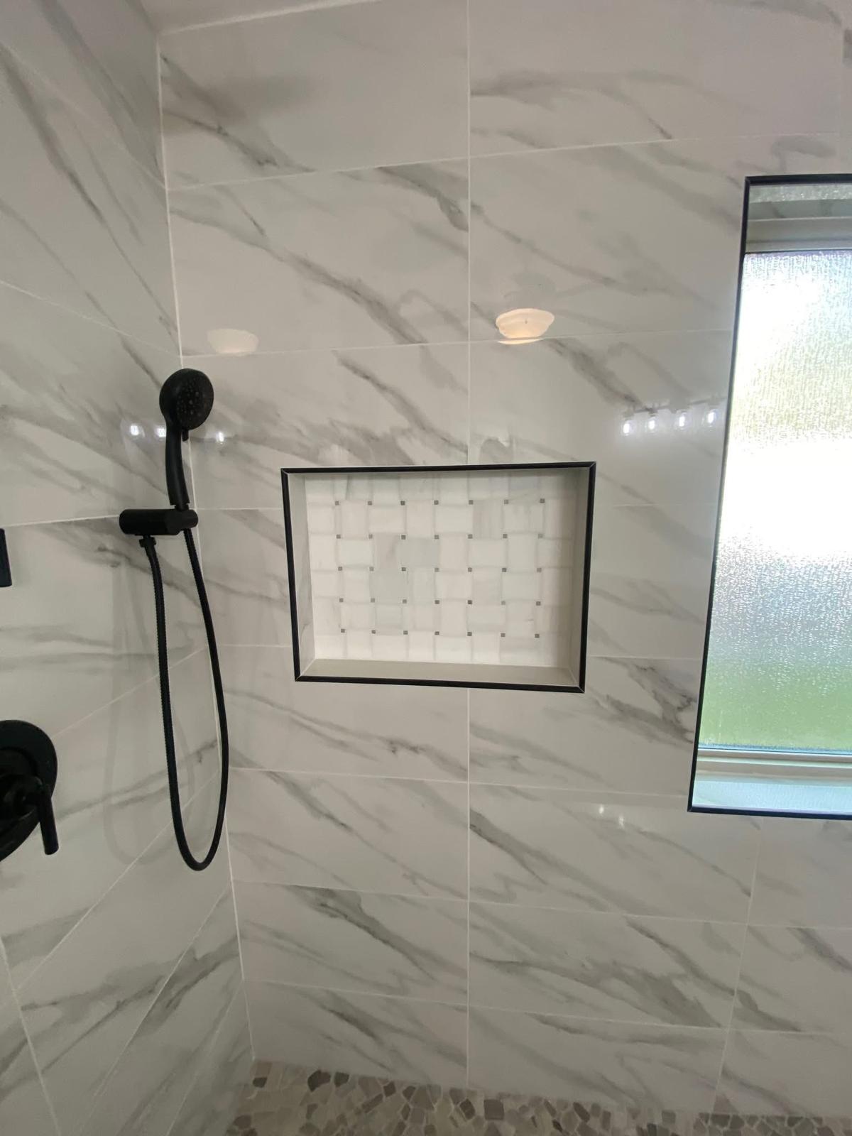 Marble-look shower with mosaic niche Marble-look shower wall with recessed niche and custom tilework in a Richmond TX bathroom remodel