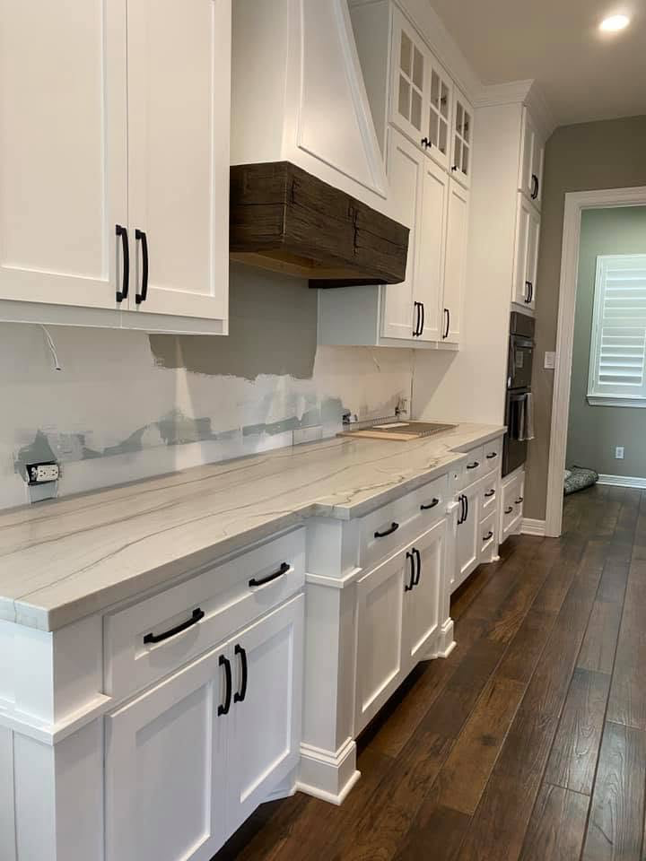 White kitchen with reclaimed wood hood White shaker kitchen with reclaimed wood range hood, quartzite counters, and matte black hardware in Fulshear TX