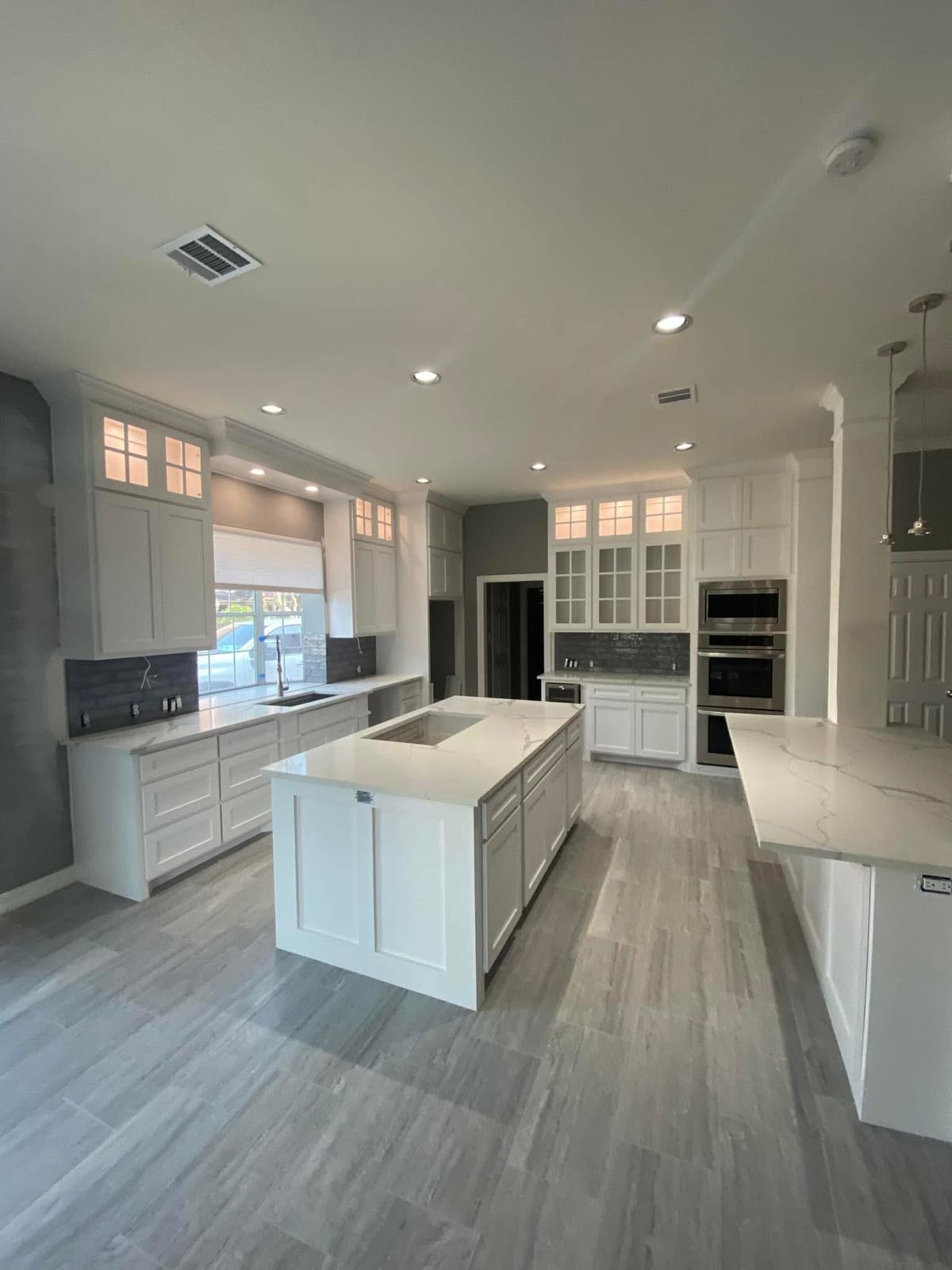 Two-island kitchen with Calacatta counters Large white kitchen with integrated appliances and Calacatta quartz islands in Fulshear TX